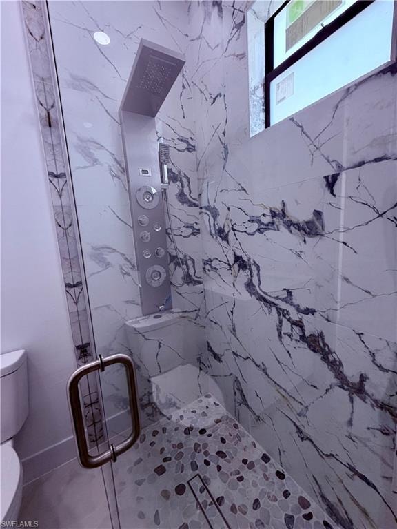 Shower enclosure featuring large format white tiled walls with dark veining, a multi-function shower panel with an overhead rainfall fixture, a built-in shower bench, and a pebble-mosaic floor