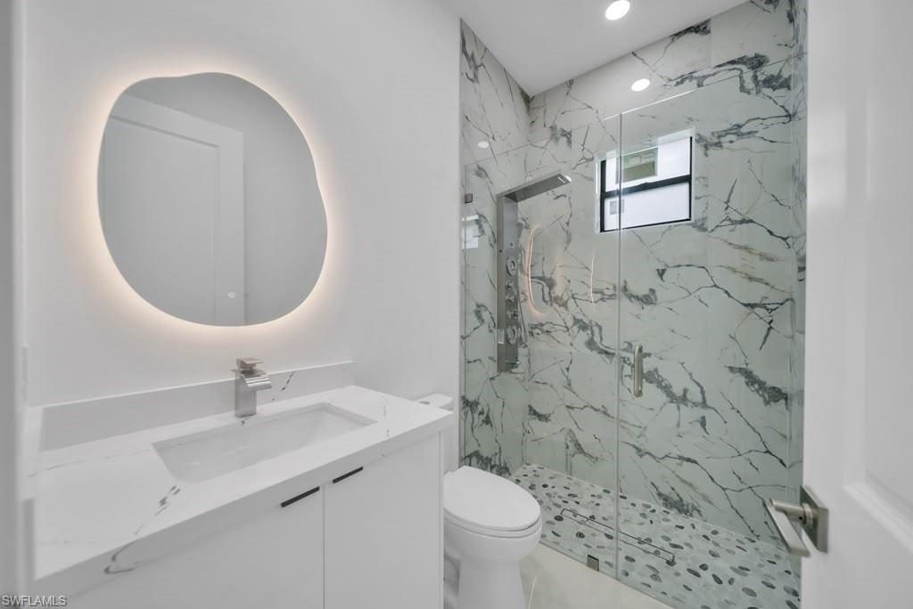 Modern bathroom featuring a custom-shaped backlit mirror, white vanity with integrated sink, and a shower enclosure with floor-to-ceiling marble-look tile