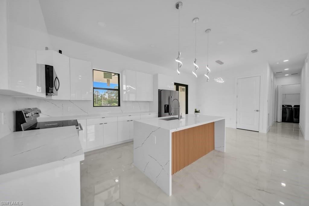 Modern kitchen featuring a waterfall island with wood slat detailing, undermount sink, and three pendant lights