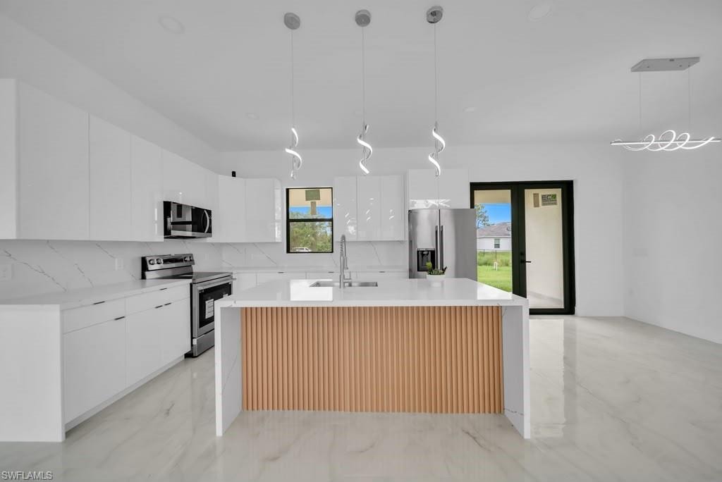 Modern kitchen featuring a white center island with wood slat detailing, white cabinetry, integrated stainless steel appliances, and large format tile flooring