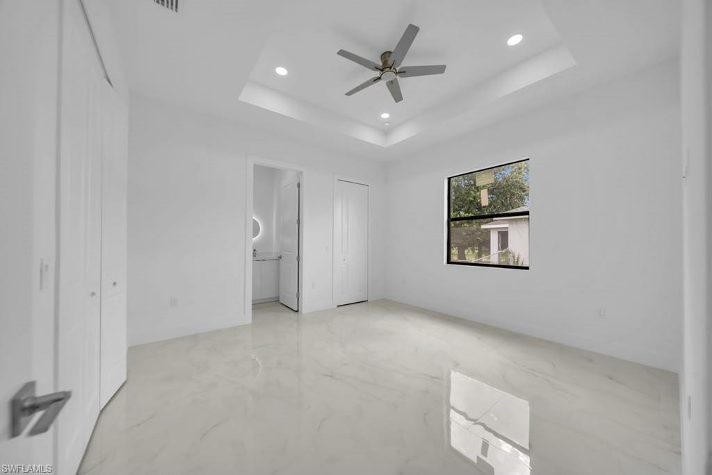 Bright interior space featuring large format tile flooring, a tray ceiling with recessed lighting, and a ceiling fan