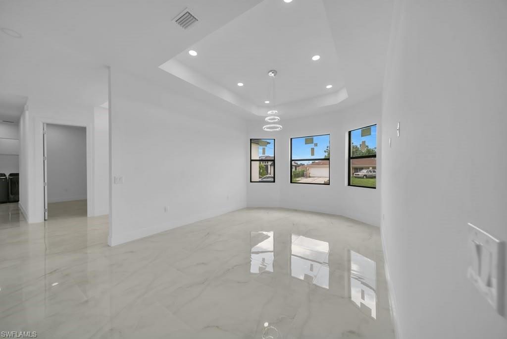 Spacious room featuring large format tile flooring, a curved wall, three transom windows, a tray ceiling with recessed lighting, and a contemporary chandelier