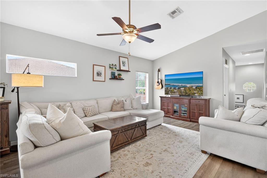 Spacious living area featuring vaulted ceilings, wood-finish flooring, a ceiling fan, and built-in floating shelves