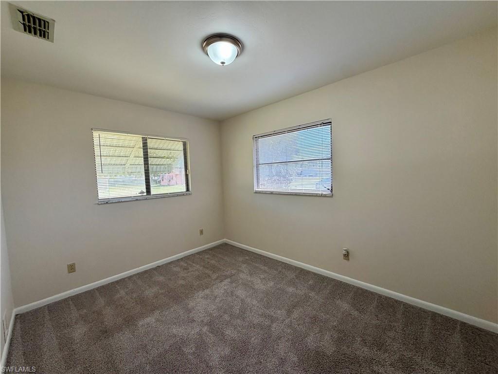 Room featuring neutral wall tones, textured carpeting, and two windows with horizontal blinds