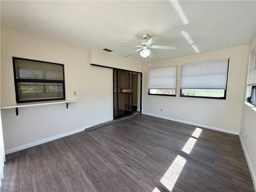 Spacious room featuring wood-finish flooring, a ceiling fan, and multiple windows with blinds