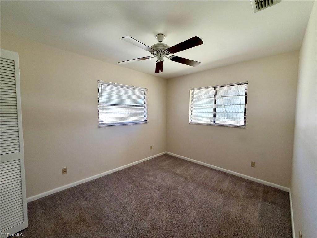 Carpeted interior room featuring a ceiling fan with wood-finish blades, two windows with blinds, a louvered bi-fold door, and light-toned walls