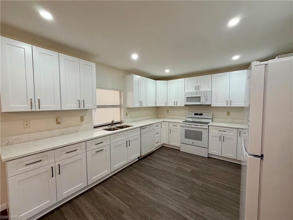 Spacious kitchen featuring white shaker-style cabinetry, light-toned countertops, wood-finish flooring, a double basin sink, and recessed lighting