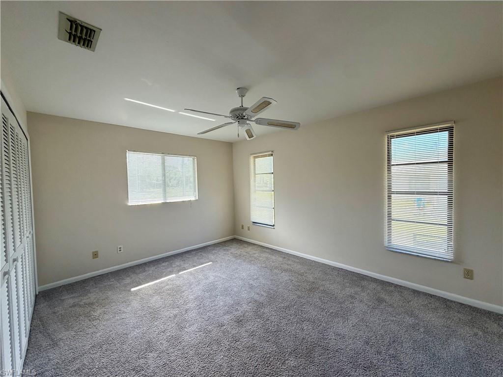 Carpeted room featuring multiple windows with blinds, a ceiling fan with light fixture, and a built-in closet with louvered bifold doors