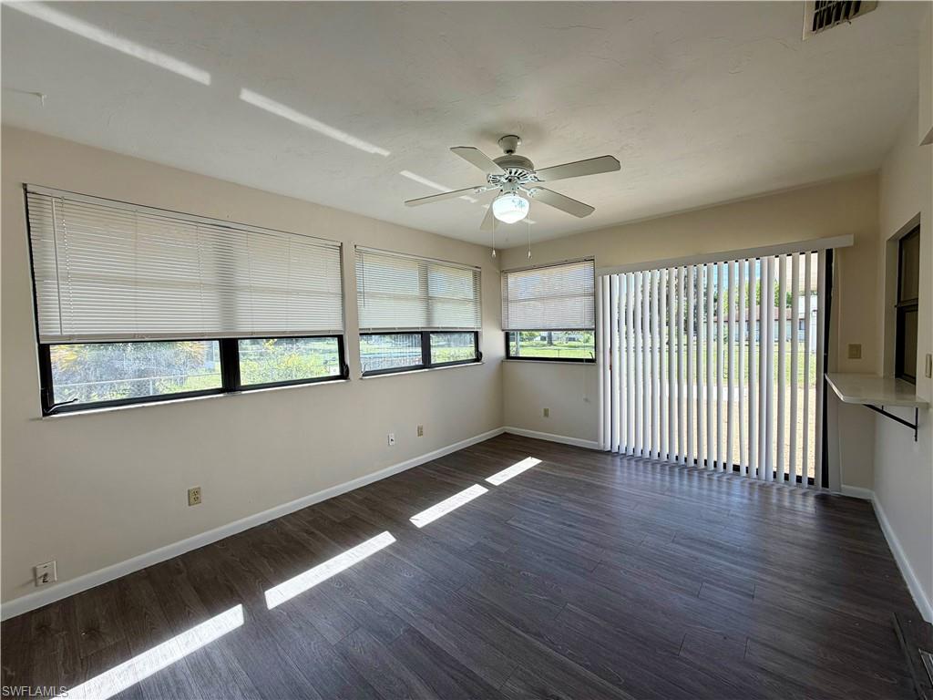 Expansive room featuring wood-finish flooring, multiple windows with blinds, a ceiling fan, and sliding glass door access to the exterior