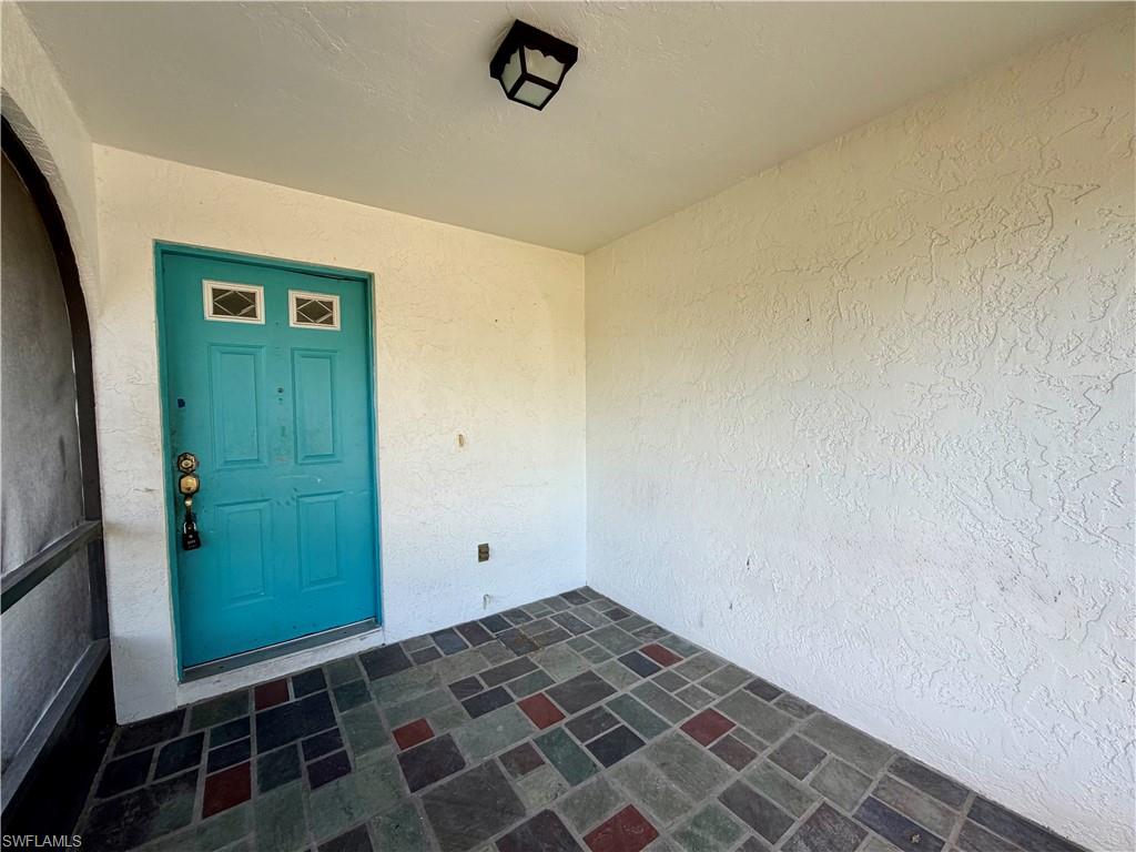 Covered entryway featuring multi-toned square floor tiling and an overhead light fixture
