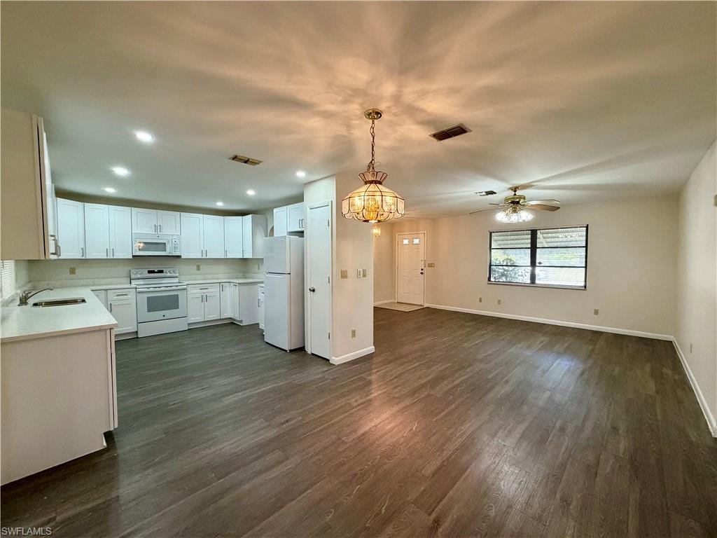 Open-concept interior featuring wood-finish flooring, a full kitchen with white cabinetry and appliances, and recessed lighting