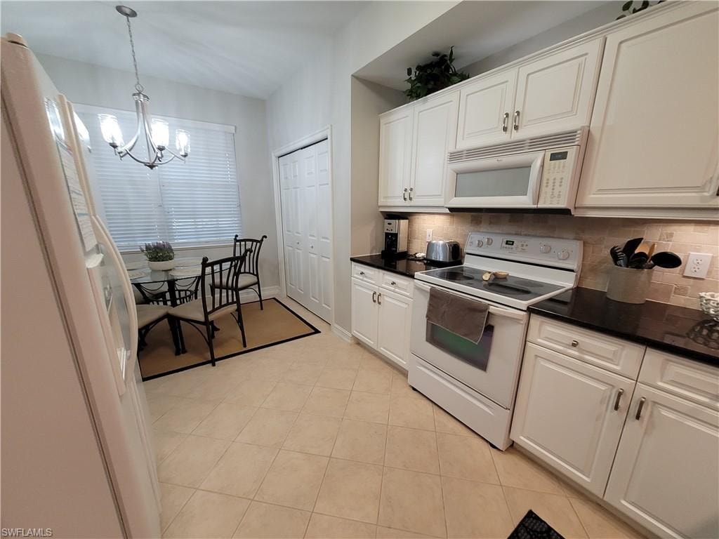 Kitchen with decorative light fixtures, white appliances, backsplash, and light tile flooring