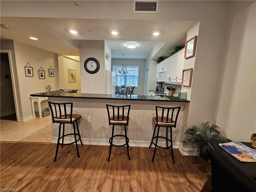 Kitchen with white appliances, wood finished floors, white cabinets, and a kitchen breakfast bar
