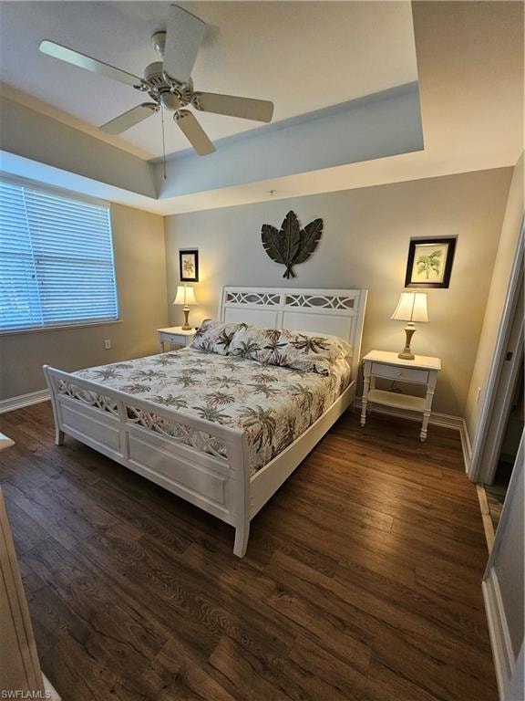 Bedroom with a raised ceiling, dark wood-style floors, and ceiling fan