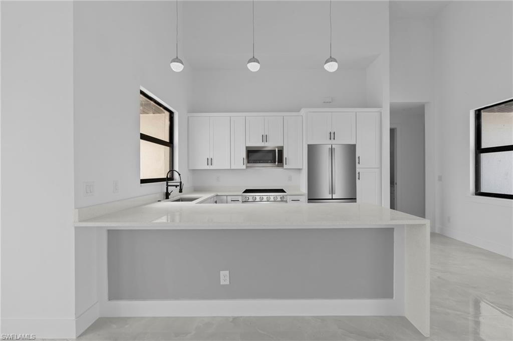 Kitchen with white cabinetry, appliances with stainless steel finishes, sink, and pendant lighting