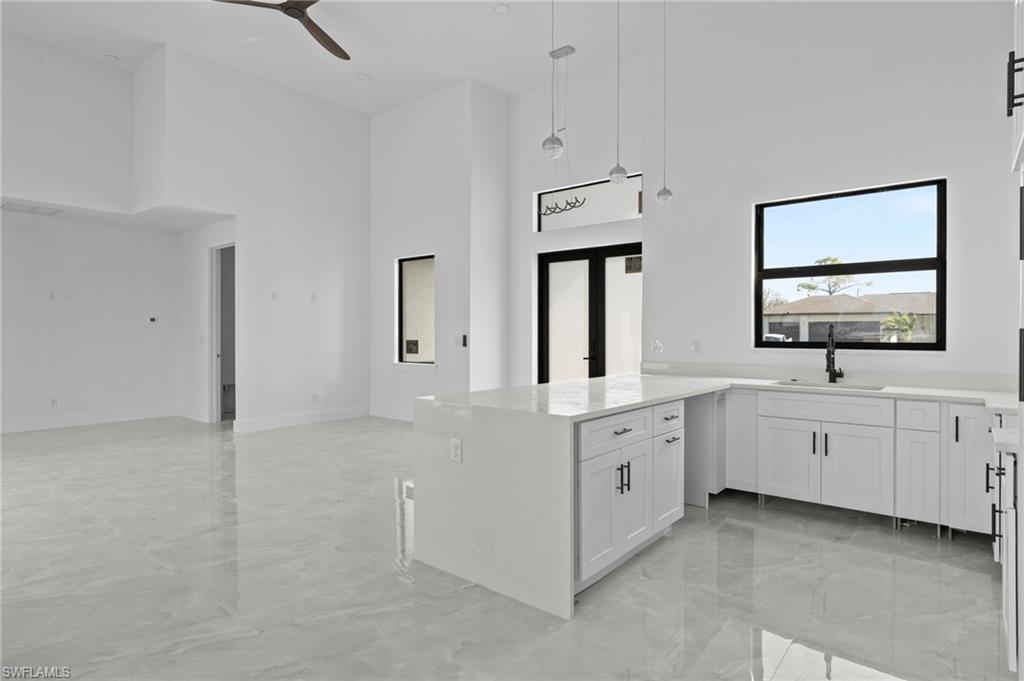 Kitchen featuring a high ceiling, white cabinetry, sink, and decorative light fixtures