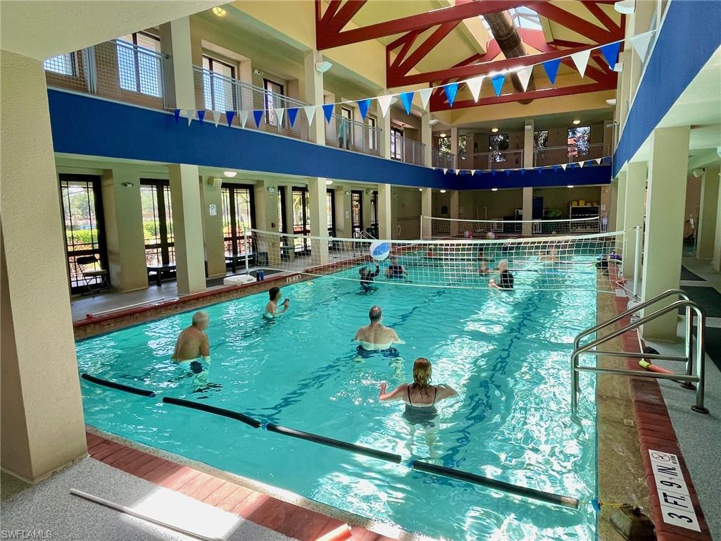Indoor swimming pool featuring a volleyball net, overhead skylights, and multi-level architectural design with walking track balcony