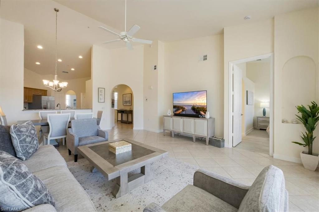 Living room featuring high vaulted ceiling, arched walkways, light tile patterned floors, a chandelier, and a ceiling fan
