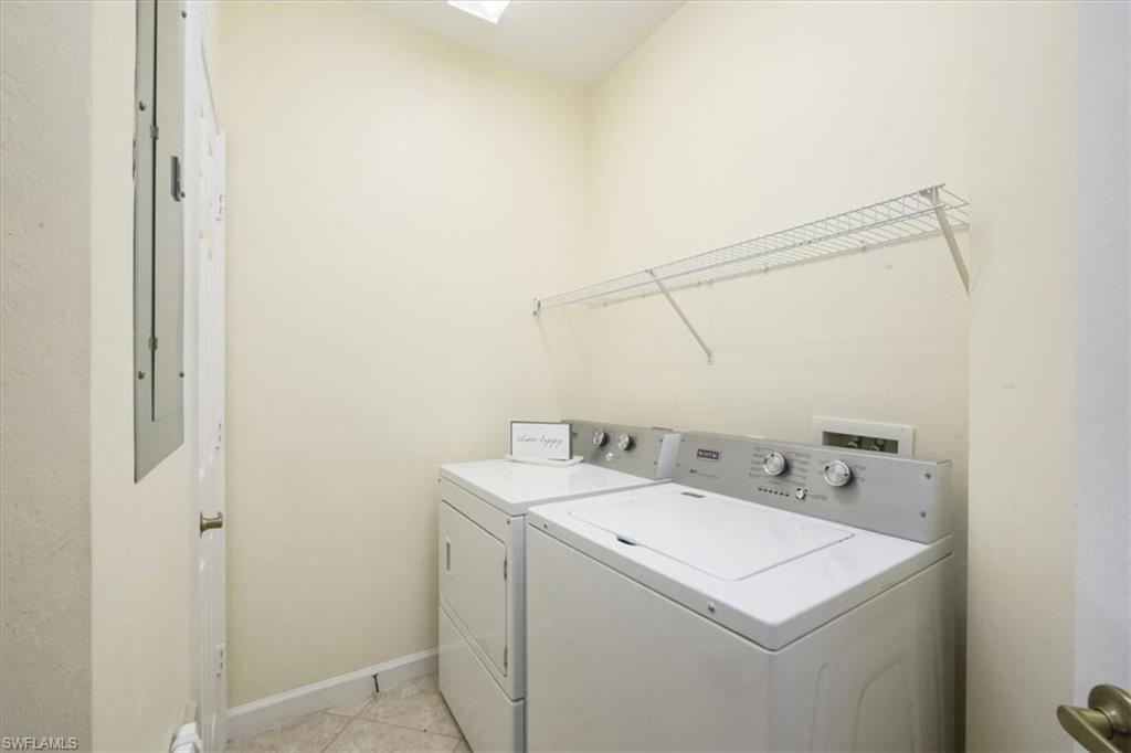 Washroom with washing machine and clothes dryer, light tile patterned flooring, and a skylight