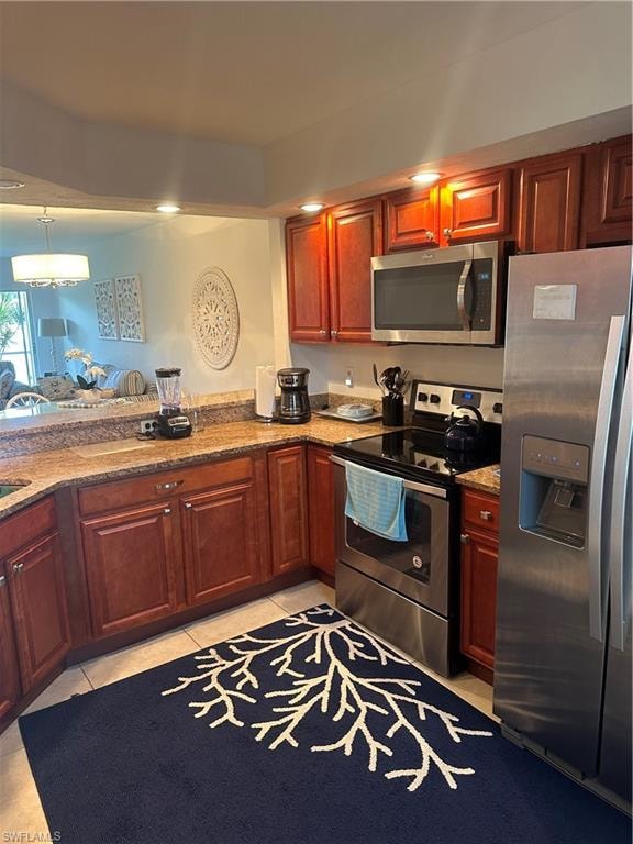 Kitchen featuring decorative light fixtures, light tile patterned floors, fridge, range, and light stone counters
