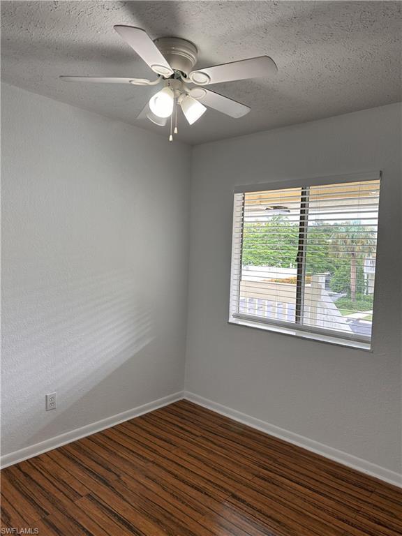Unfurnished room with dark wood finished floors, a textured ceiling, a textured wall, and a ceiling fan