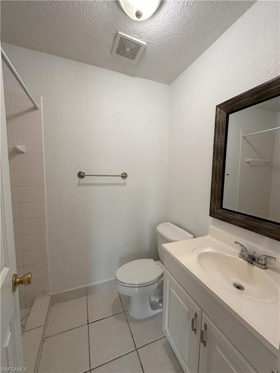 Bathroom with vanity, light tile patterned floors, tiled shower, a textured ceiling, and a textured wall