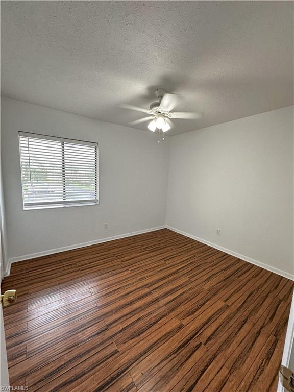 Unfurnished room with a textured ceiling, dark wood finished floors, and a ceiling fan