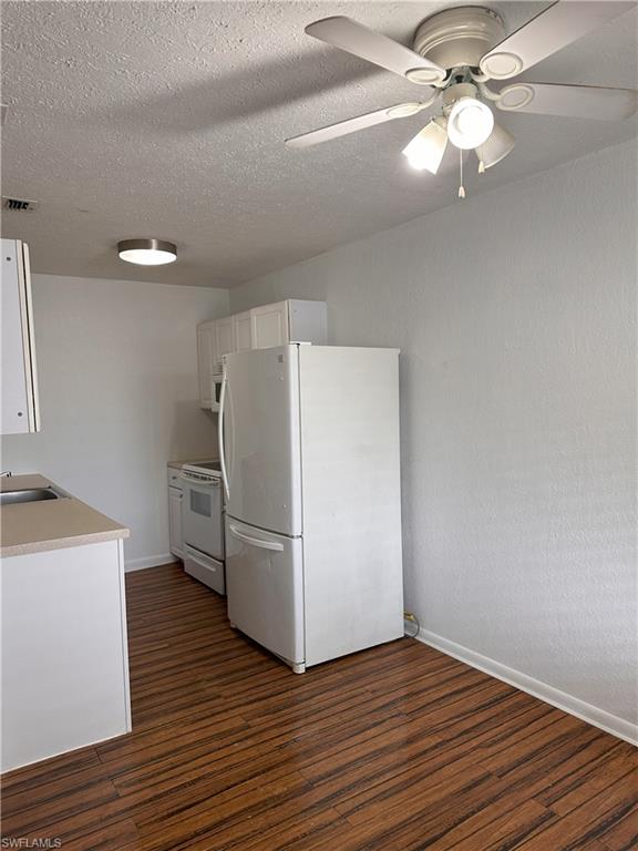 Kitchen featuring white cabinetry, white appliances, light countertops, dark wood-type flooring, and ceiling fan