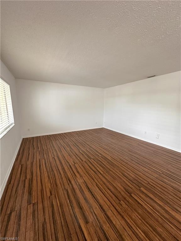 Empty room featuring a textured ceiling and dark wood-style floors
