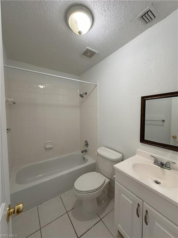 Full bathroom with light tile patterned floors, vanity, bathing tub / shower combination, a textured ceiling, and a textured wall