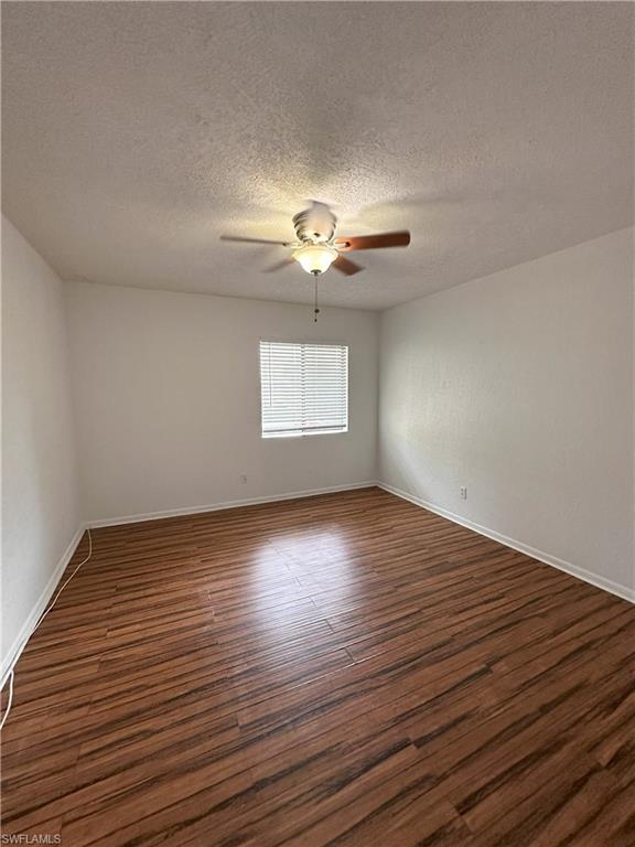 Empty room featuring dark wood-style flooring, a textured ceiling, and a ceiling fan