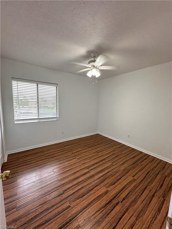 Spare room featuring a textured ceiling, dark wood-type flooring, and a ceiling fan