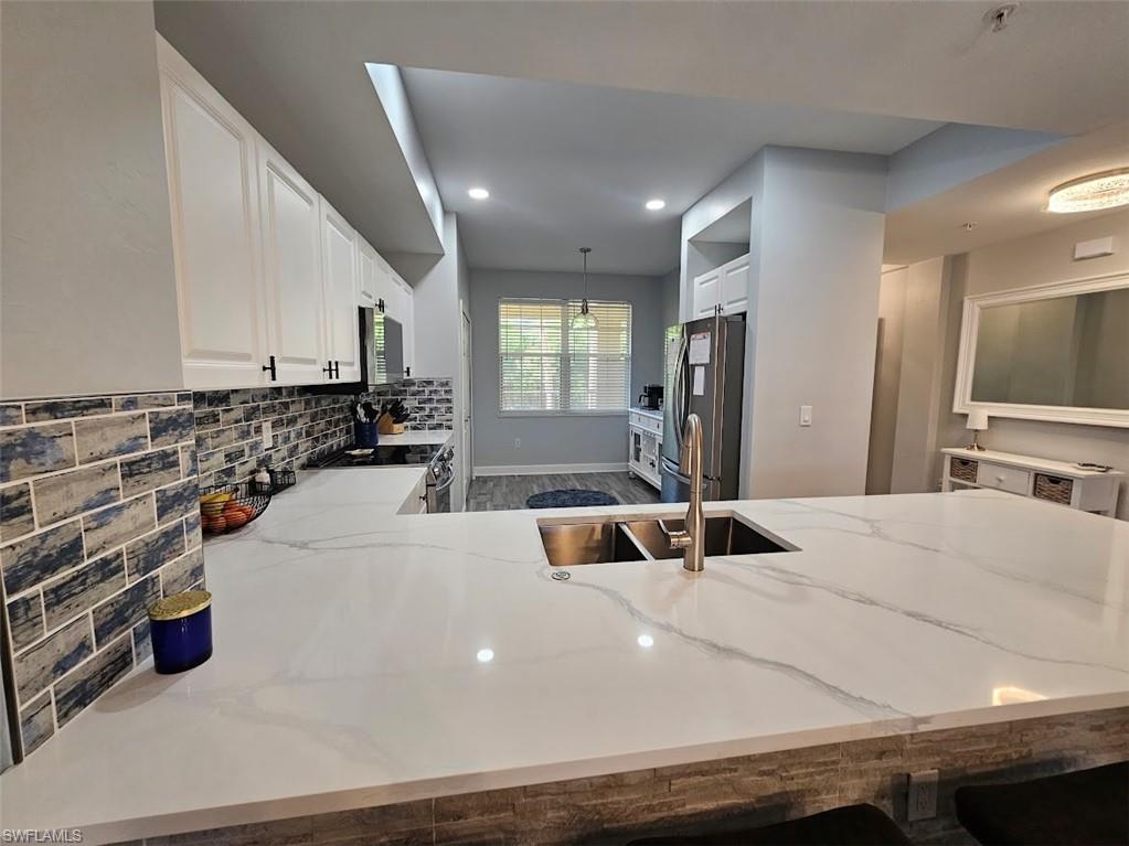 Kitchen featuring stainless steel appliances, light stone countertops, white cabinetry, and decorative backsplash