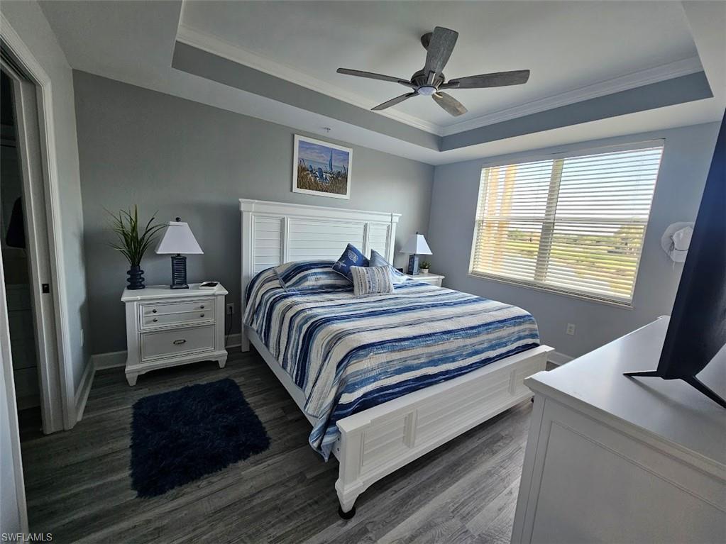 Bedroom featuring a tray ceiling, dark wood finished floors, a ceiling fan, and ornamental molding
