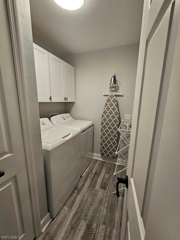 Washroom featuring dark wood-type flooring, washing machine and clothes dryer, baseboards, and cabinet space