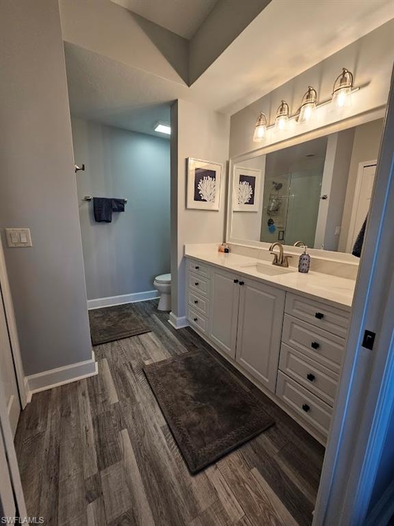 Bathroom featuring baseboards, toilet, vanity, wood finished floors, and a shower with shower door