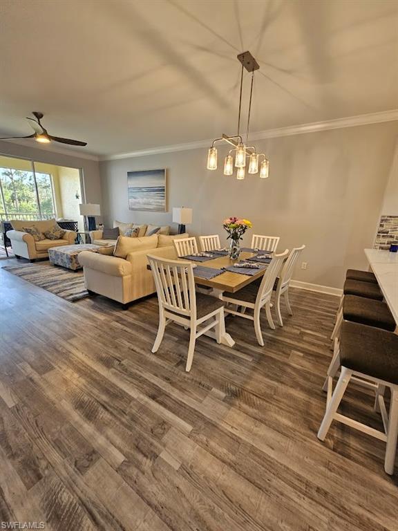 Dining area with dark wood-type flooring, baseboards, ornamental molding, and a ceiling fan
