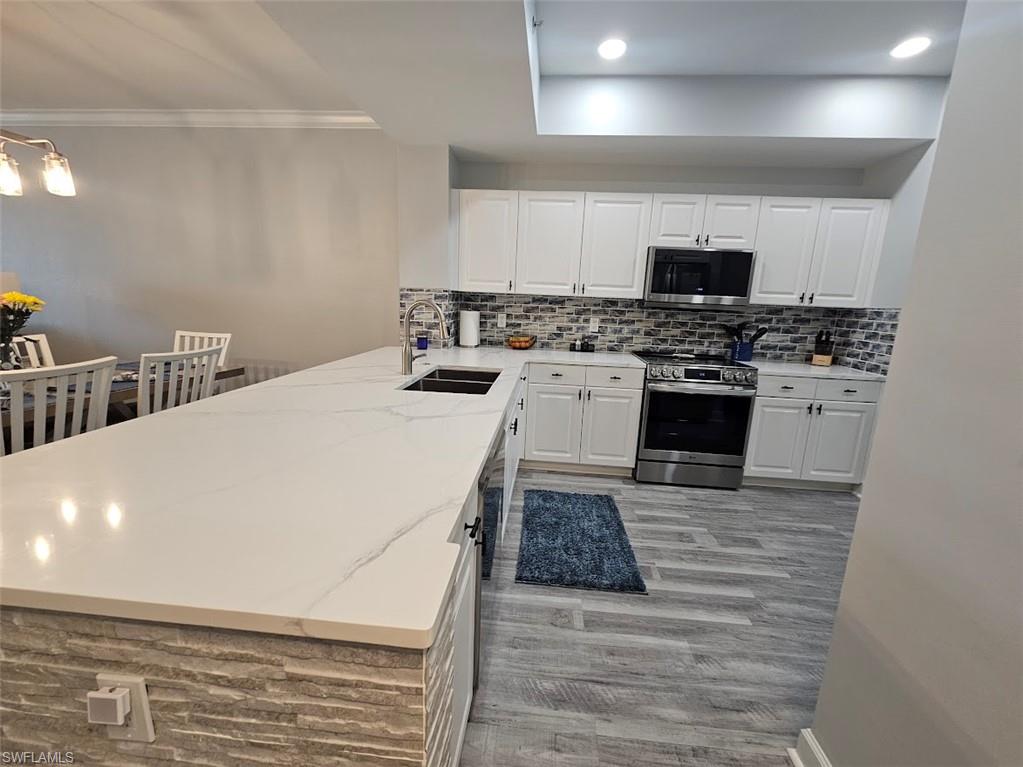 Kitchen with ornamental molding, a peninsula, stainless steel appliances, light wood finished floors, and a sink