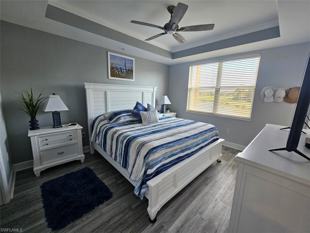 Bedroom with baseboards, a raised ceiling, dark wood-style flooring, ceiling fan, and crown molding