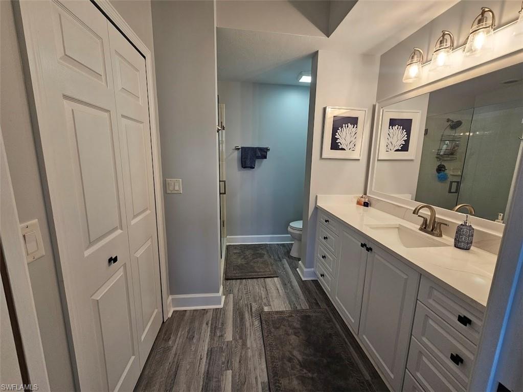Full bath featuring vanity, baseboards, toilet, a shower stall, and wood finished floors