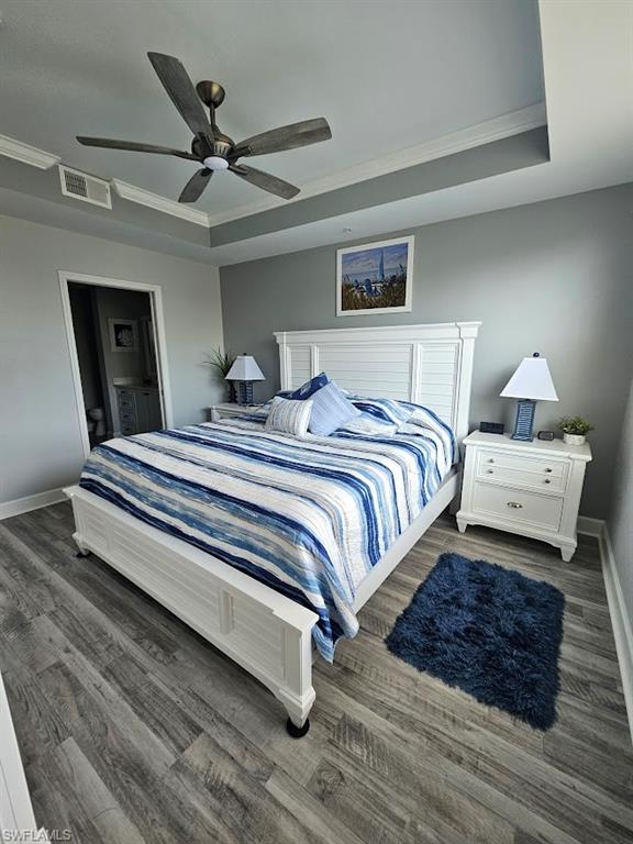 Bedroom featuring visible vents, baseboards, a raised ceiling, crown molding, and wood finished floors