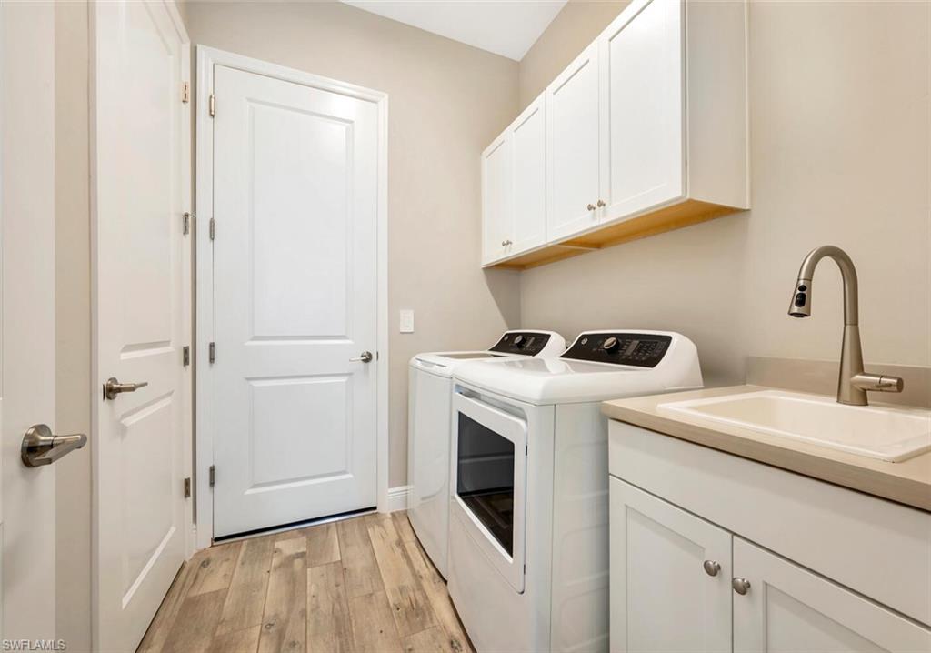 Clothes washing area featuring sink, washing machine and clothes dryer, light hardwood / wood-style flooring, and cabinets