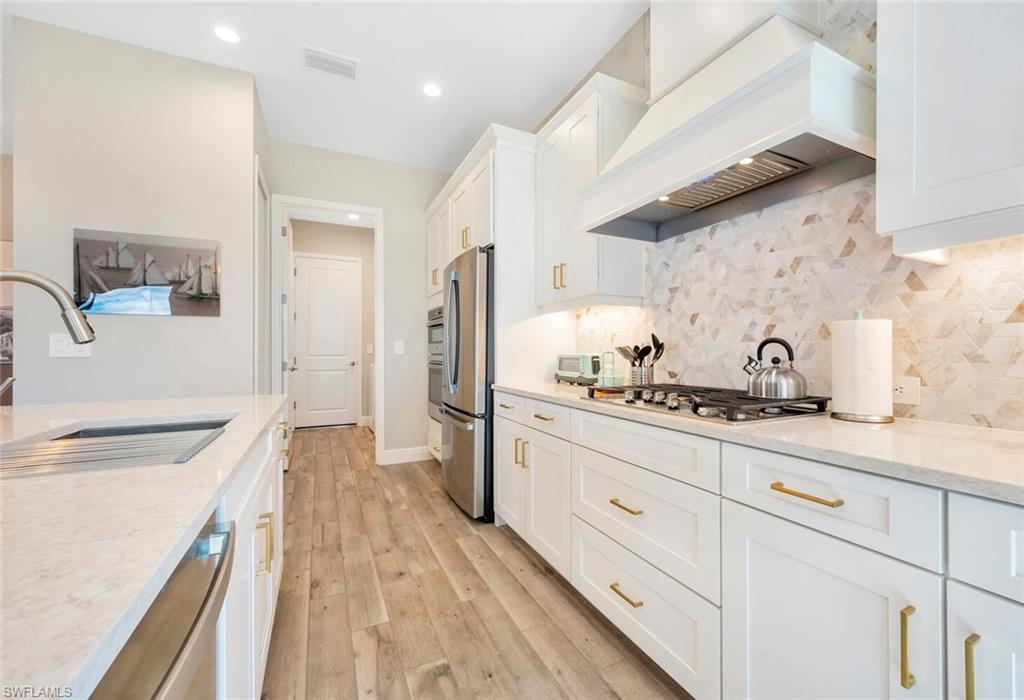 Kitchen featuring light hardwood / wood-style floors, backsplash, stainless steel appliances, white cabinets, and premium range hood