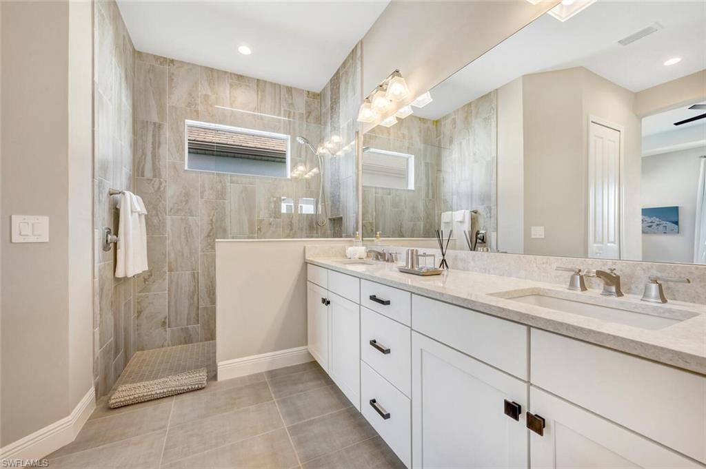 Bathroom with dual sinks, tiled shower, tile floors, a wealth of natural light, and large vanity