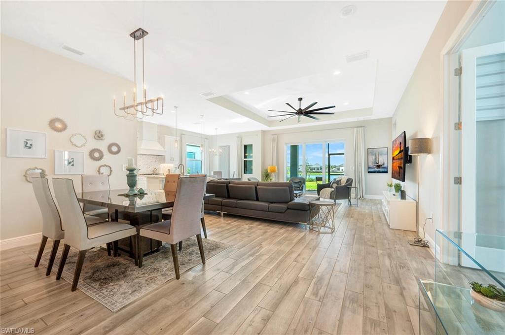 Dining area with a tray ceiling, ceiling fan with notable chandelier, and light hardwood / wood-style flooring