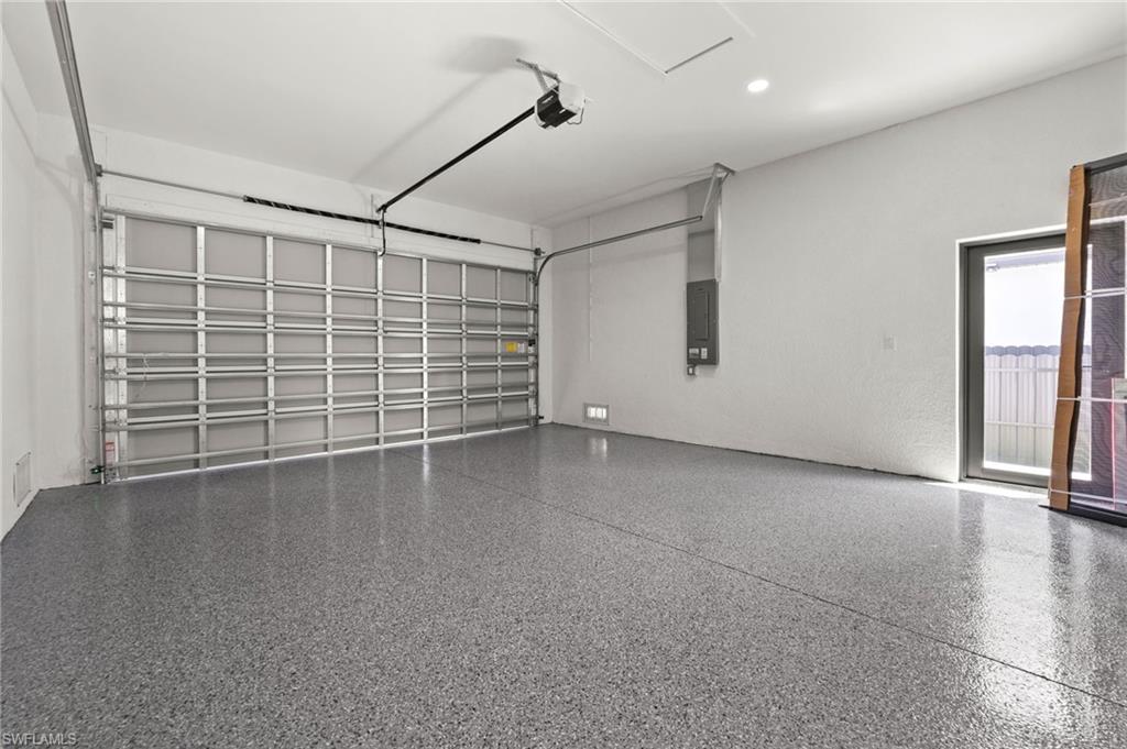 Spacious garage featuring a durable epoxy-coated floor, automatic overhead door opener, recessed lighting, and a frosted glass pedestrian door