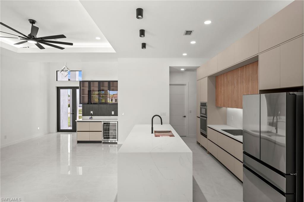 Modern kitchen featuring a large center island with integrated sink, sleek flat-panel cabinetry, built-in stainless steel appliances, and wood-finish accents