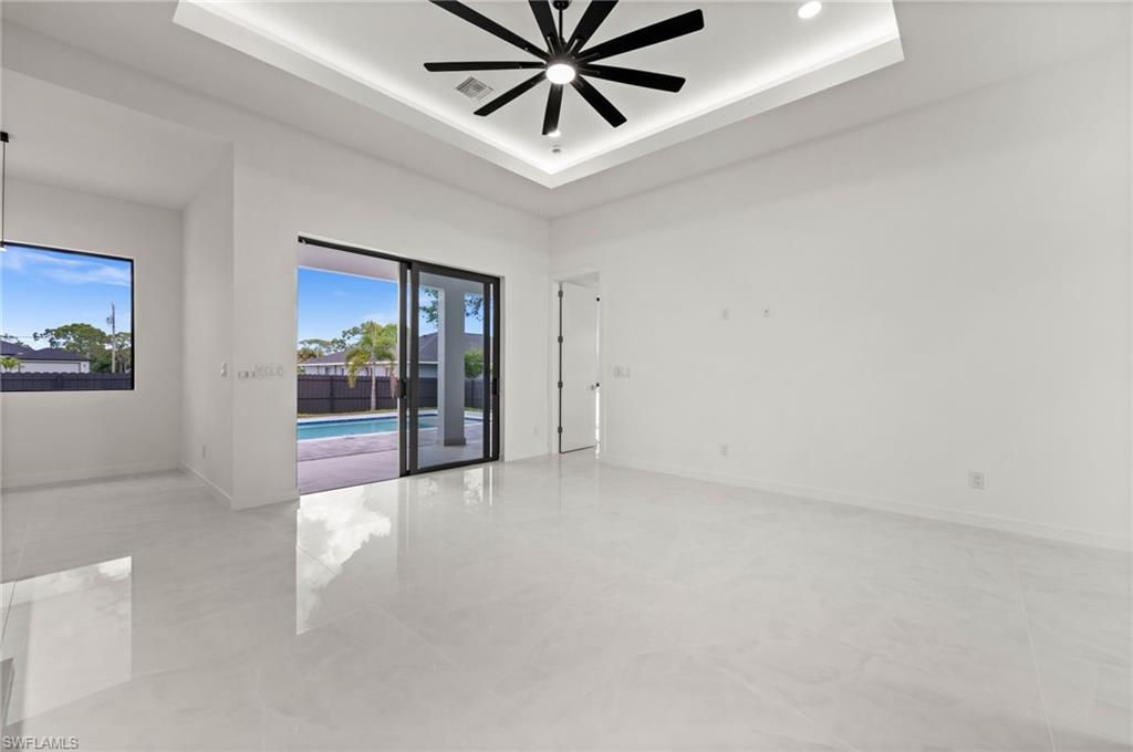 Spacious interior featuring large format tile flooring, a tray ceiling with recessed lighting, and a modern ceiling fan