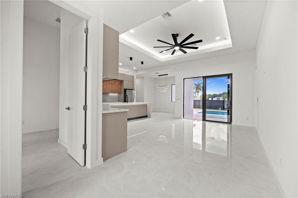 Spacious interior featuring large format tile flooring, a modern kitchen with two-tone cabinetry and an island, a tray ceiling with recessed lighting and a ceiling fan, and sliding glass doors opening to an outdoor area with a swimming pool