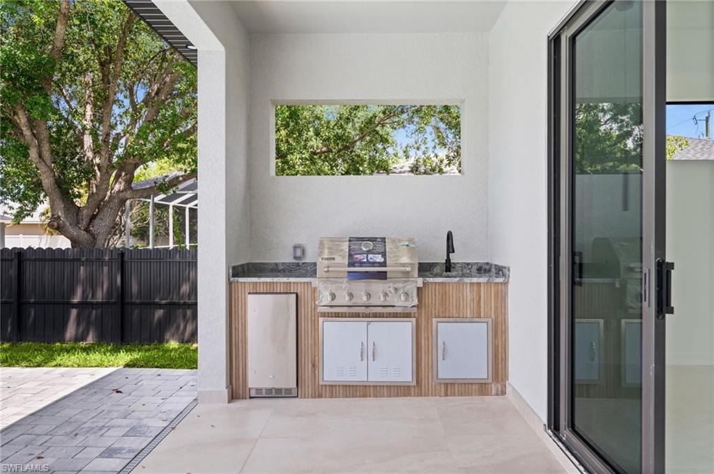 Outdoor kitchen featuring a built-in grill, integrated sink with a matte black faucet, and a stone-finish countertop